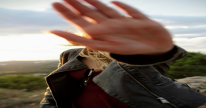 Picture of what appears to be a woman wearing a what appears to be a leather jacket hiding her face from the camera with her hand. Human Trafficking Traffickers