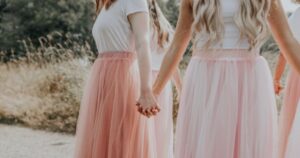 The photo depicts a group of women or girls holding hands, standing outdoors in a natural setting. They are wearing matching pink tulle skirts and white tops, giving a sense of unity and togetherness. The image has a soft, harmonious feel, with the focus on the connection between the individuals. There is a growing trend in Human Trafficking Convictions.